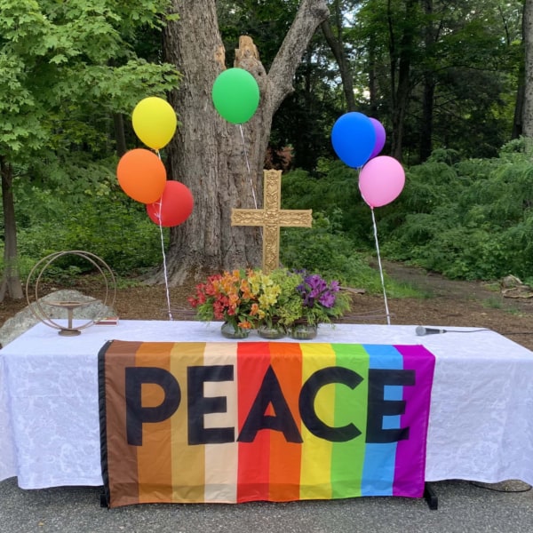 Close up of worship altar with rainbow balloons and rainbow flag that says "Peace."